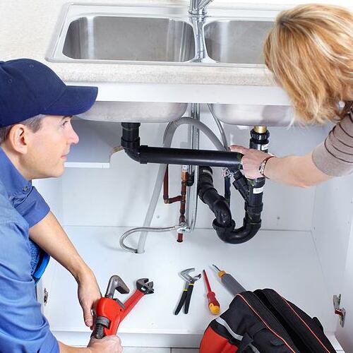 A Plumber Takes Care of Plumbing under a Sink.